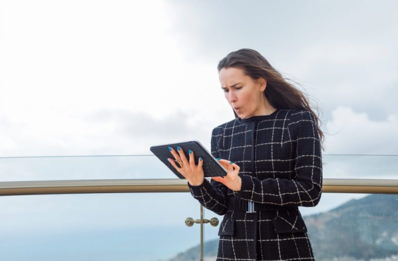 Surprised blogger girl is looking at planshet computer in hand against the background of city view.